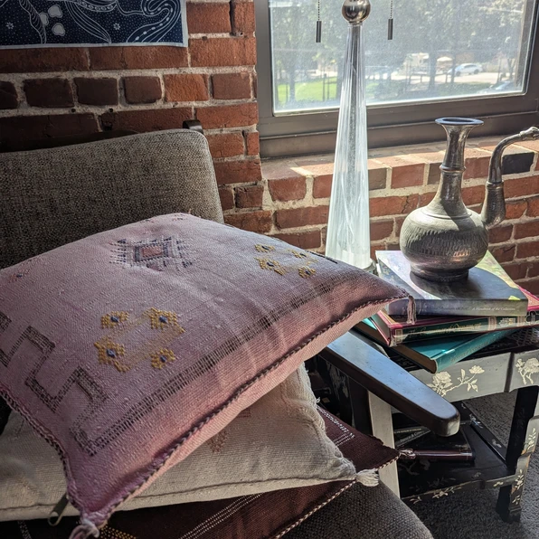 Pink Amina Moroccan cactus silk throw pillow with embroidered motifs, styled on a chair stacked with white and brown cushions