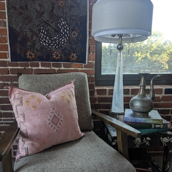 Amina Moroccan cactus silk throw pillow in soft pink with geometric embroidery, displayed on a modern chair with brick wall,