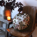 decorative circular throw pillow with velvet pink and green floral designs on a wicker chair