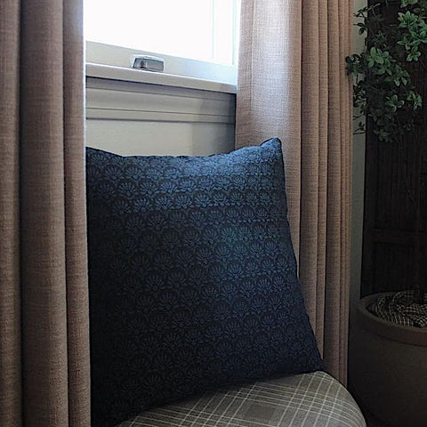 Square accent throw pillow with a dark blue geometric design and black velvet backing in a chair