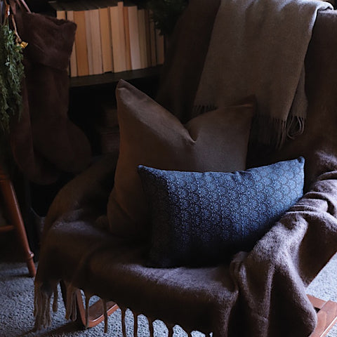 Lumbar accent throw pillow with a dark blue geometric design in a chair by bookshelf