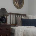 dark blue lumbar throw pillow layered with other pillows on bed next to side table