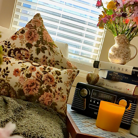 pink and green velvet throw pillows on living room couch with record player and books on side table